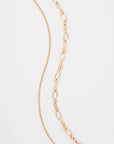 Two Alba Glasses Chains by For Art's Sake® are placed against a white background. The chain on the left, an 18K gold-plated piece, features a delicate, thin design with evenly spaced links. The chain on the right is composed of larger, oval links arranged in a slightly tapered pattern.