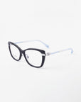 The Amour by For Art's Sake® features black cat-eye frames with clear lenses, silver hinge details, and light blue temples. Adjustable nose pads offer all-day comfort. Shown on a white background for an elegant display.