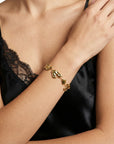 A person in a black satin top with lace trim rests their hand on their shoulder, showcasing the chunky modern For Art's Sake® The Forms Bracelet with irregular links on their wrist.