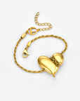 The Puffy Heart Bracelet by For Art's Sake® features a twisted gold chain with two shiny, smooth heart-shaped charms and a lobster clasp, displayed on a plain light background.