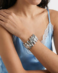 A person wearing a sleeveless light blue satin top with lace trim poses with crossed arms, showcasing The Forms Bangle by For Art's Sake®—a bold, sculptural modern accessory on their wrist.