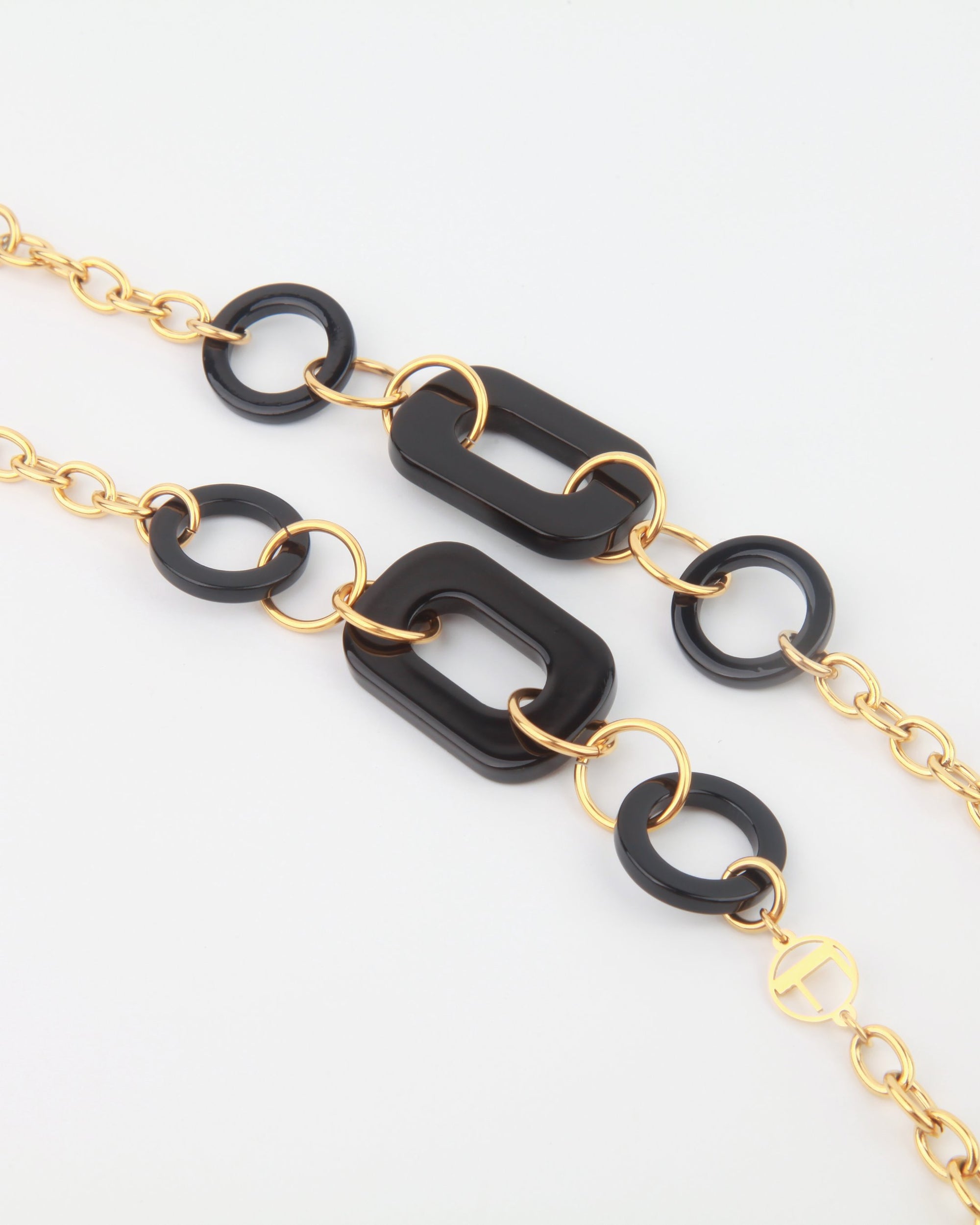 A fashionable NYC Glasses Chain featuring alternating black geometric links and 18-karat gold-plated chain links, creating a bold and stylish accessory. The black acetate links, in a mix of rectangular and circular shapes, are connected by smaller gold loop links. The overall For Art's Sake® aesthetic is modern and chic.