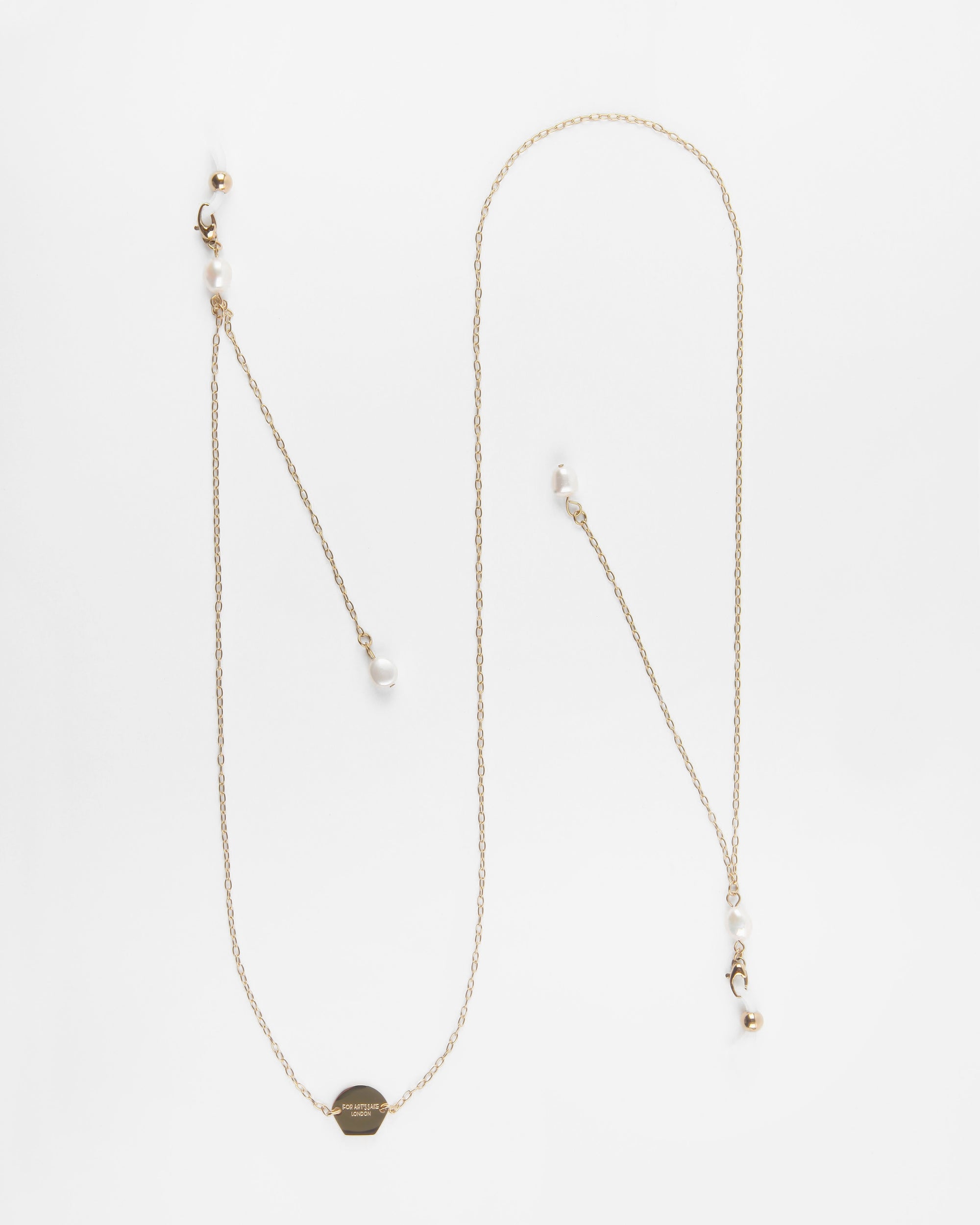 A delicate Victoria Glasses Chain from For Art's Sake® with freshwater pearl accents lies uncoiled on a white surface. The 18K gold chain features a small, round pendant with an engraved design. Multiple strands of the chain boast dispersed pearl and gold bead details along its length.