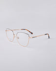 The Dora frames by For Art's Sake® showcase metal-rimmed eyeglasses with sleek, gold-colored designs set against a simple light backdrop. The temples feature a sturdy stainless steel core adorned with a tortoiseshell pattern, and the clear, slightly oversized lenses are equipped with a blue light filter for contemporary eye protection.