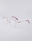 The Dora frames from For Art's Sake® showcase a sleek, metallic gold design with maroon temple tips set against a plain white backdrop. Equipped with blue light filter lenses, these eyeglasses effortlessly combine minimalist and modern aesthetics.