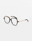 A pair of black Dumpling eyeglasses with a square frame and gold arms by For Art's Sake®. The arms have a decorative chain-like pattern. The lenses offer blue light filter protection. The glasses are placed on a white surface.