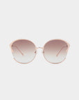 A pair of stylish For Art's Sake® Alectrona sunglasses with large, round, gradient lenses transitioning from dark to light shades. The frame is a light pink metal with a subtle cat-eye shape, featuring 18-karat gold-plated temples that are slim and matching in color. The background is white.