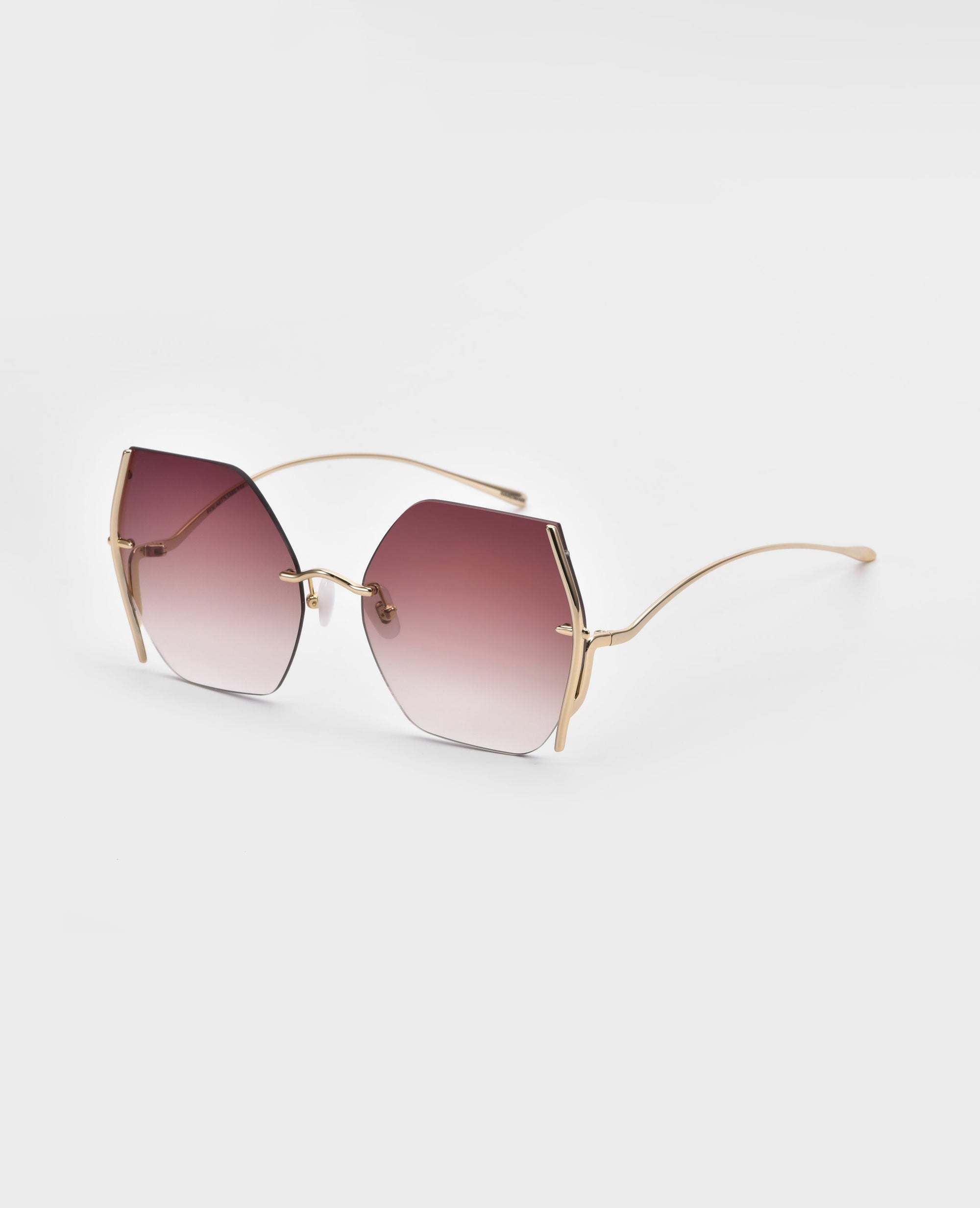 A pair of For Art's Sake® Generation sunglasses with gradient pink lenses and thin, gold-plated stainless steel frames. The lenses have an irregular hexagonal shape, and the overall design is minimalist and chic. Featuring jadestone nosepads for added comfort, these sunglasses offer UV protection against harmful rays. The background is a plain white.