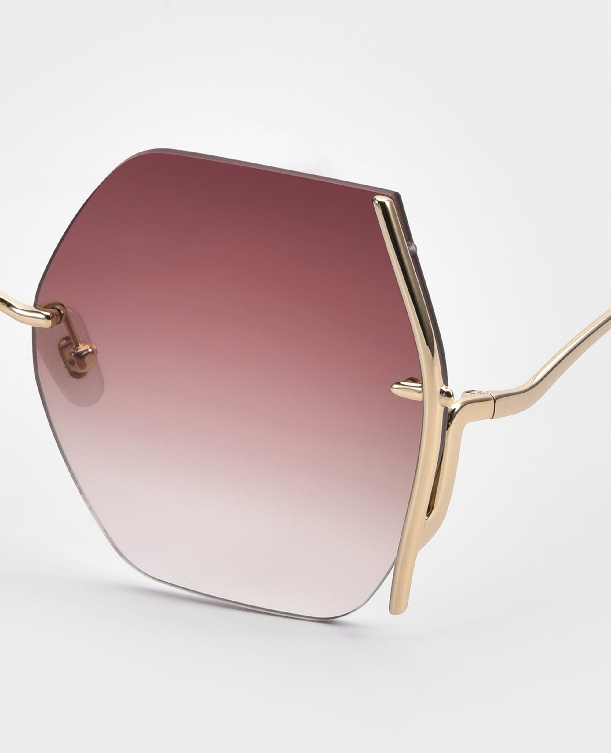 Close-up of For Art's Sake® Generation sunglasses: geometric hexagonal frames in thin gold metal, jadestone nosepads, pink gradient lenses, and essential UV protection—all showcased against a plain white background.