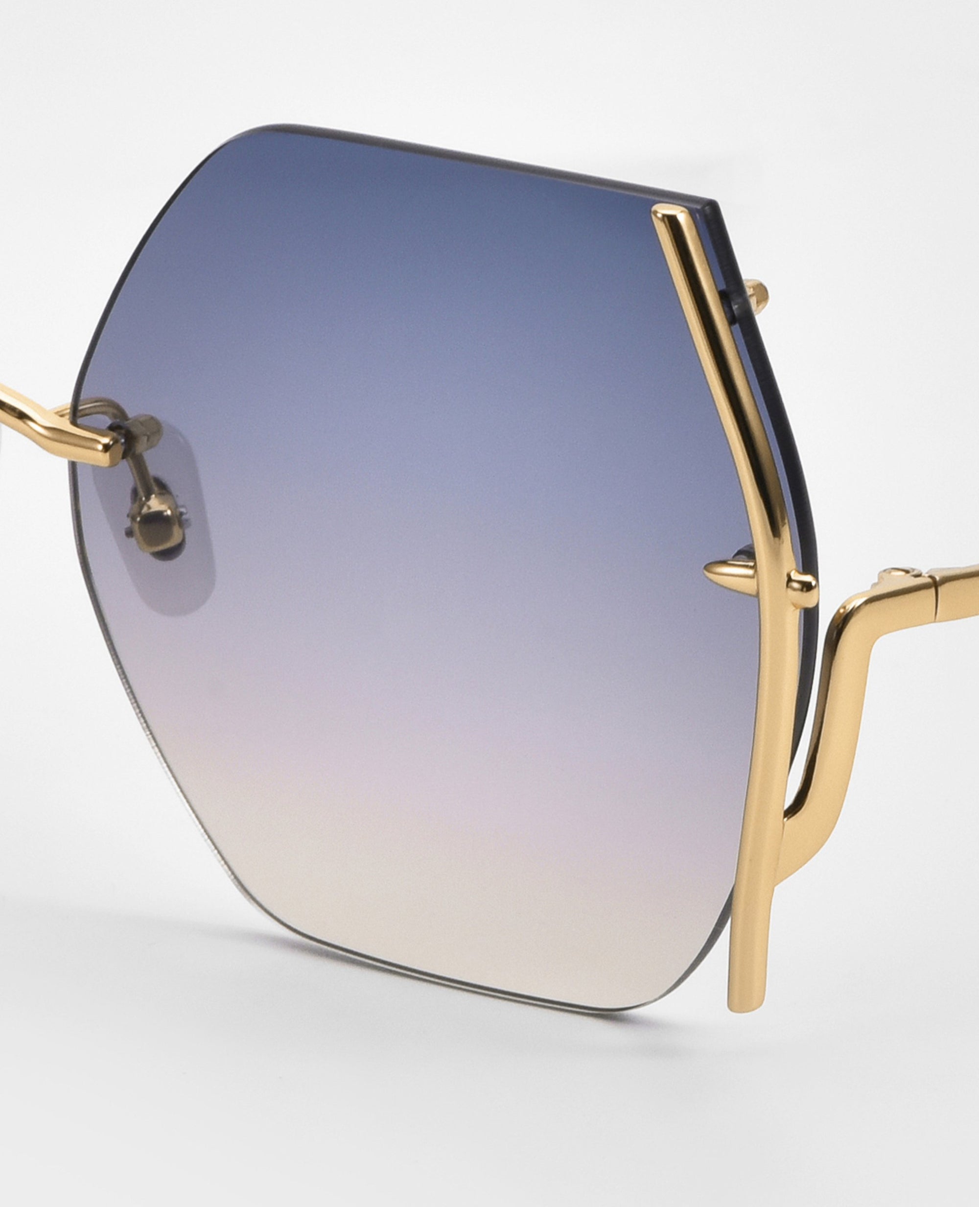 Close-up of For Art's Sake® Generation Topaz sunglasses—ONLY 1 AVAILABLE—with octagonal blue-to-clear gradient lenses and a gold, branch-like frame. A rare find for standout style and reliable UV protection.