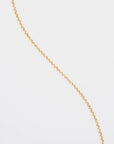 A thin, 18K gold-plated chain with small, round links is draped diagonally across a plain white background. The Florentina Glasses Chain by For Art's Sake® is simple and elegant with a slight shine.