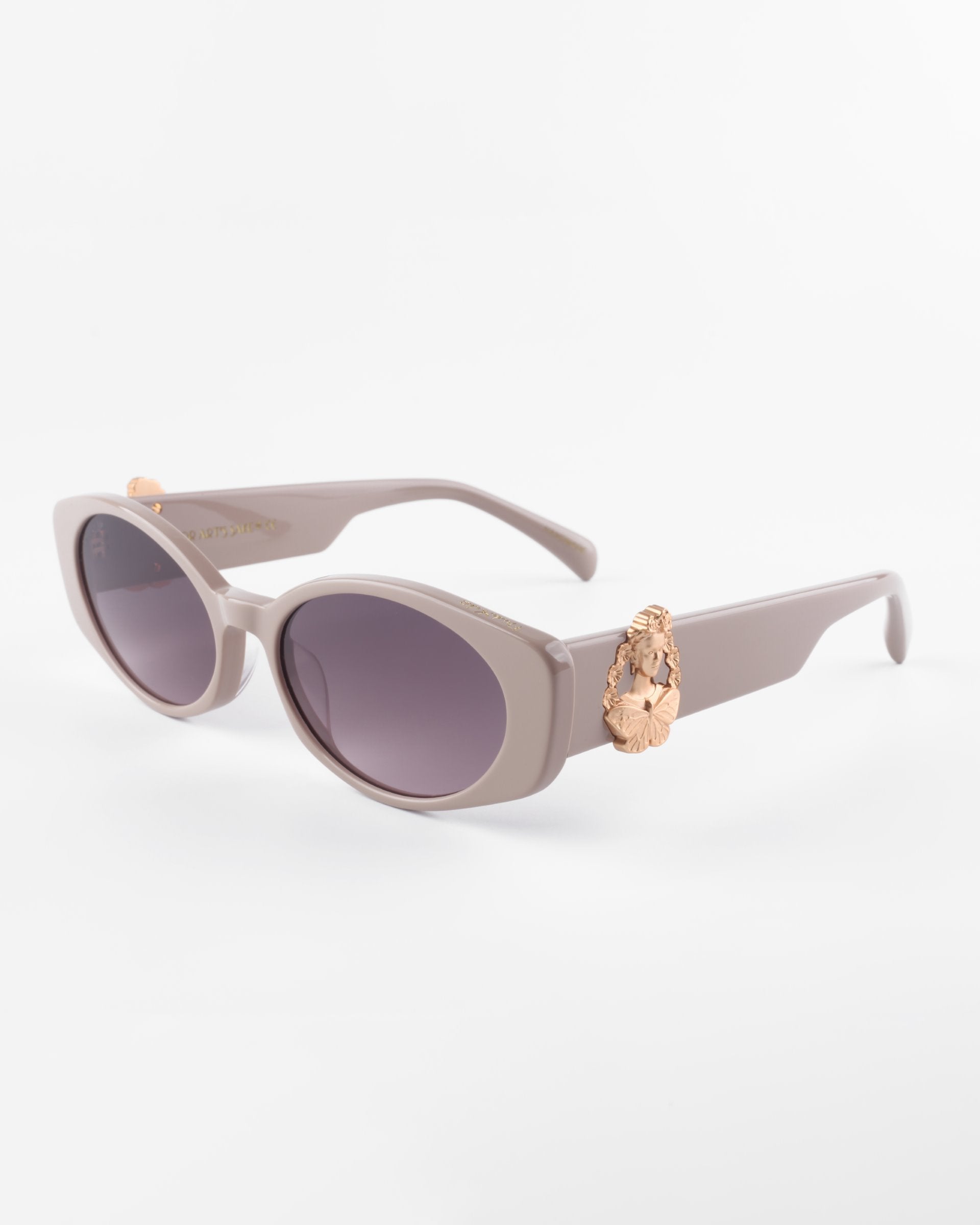 Oval-shaped, muted lavender Frida Portrait sunglasses by For Art's Sake® with ultra-lightweight nylon lenses offering 100% UVA & UVB protection. The frame features an ornate, 18-karat gold-plated decorative element on the temples near the hinges. The background is a plain white surface.