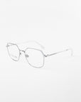 **For Art's Sake® Godiva:**
A pair of sleek, silver metal glasses with a minimalist design. The frames are thin and angular, featuring a slight geometric shape. Equipped with prescription lenses, the arms are straight with a subtle hinge near the lenses, and the nose pads are clear. The background is plain white.