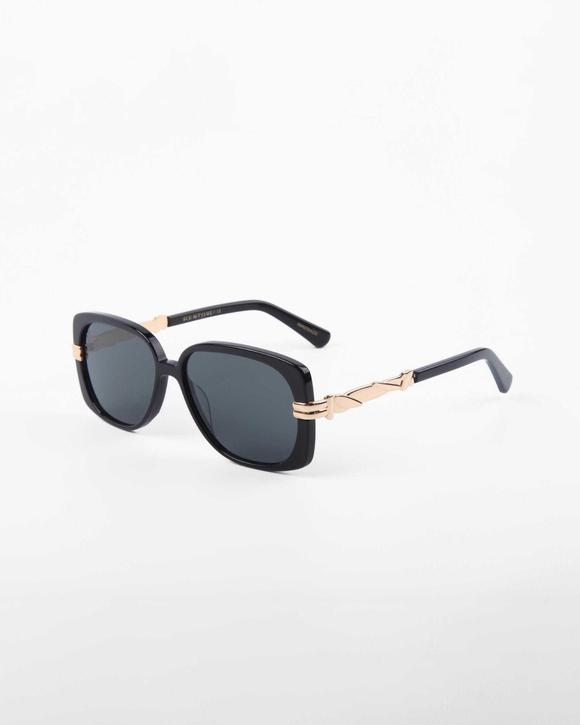 The Icon-ARC sunglasses by For Art's Sake® are handmade with sleek black acetate in a square design, featuring dark lenses and gold-accented arms. They offer full UVA & UVB protection and blend style with function, elegantly set against a plain white background.