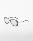 The Icon-ARC sunglasses by For Art's Sake® have square acetate frames with dark lenses and black-silver arms featuring a geometric pattern. They offer UVA & UVB protection and are showcased against a white background.