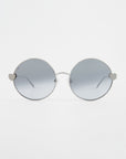 A pair of round For Art's Sake® Love Story shades with thin silver frames and grey-tinted lenses. The hinges on both sides are in the shape of small hearts, adding a unique and playful touch to the minimalist design. Equipped with jadestone nose pads, they also offer 100% UV protection against harmful rays. The background is plain white.