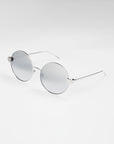 A pair of round, silver-framed sunglasses with light gray lenses is set against a white background. The frames are thin and minimalist, with slightly curved temples and jadestone nose pads. These For Art's Sake® Love Story shades also offer 100% UV protection for both style and safety.