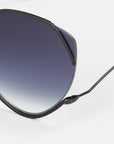 Close-up of For Art's Sake® Wonderland sunglasses with thin black metal frames, jadestone nose pads, and large blue gradient lenses with 100% UV protection. Only a section of one lens and the frame arm appear against a white background.