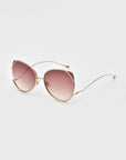 The Wonderland cat-eye sunglasses by For Art's Sake® feature gold frames, jadestone nose pads, and gradient pink lenses with 100% UV protection, shown on a plain light gray background.