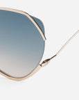 Close-up of For Art's Sake® Wonderland sunglasses with gold frames and blue gradient lenses, offering superior UV protection. Set against a white background, only one lens and part of the frame and arm are visible.