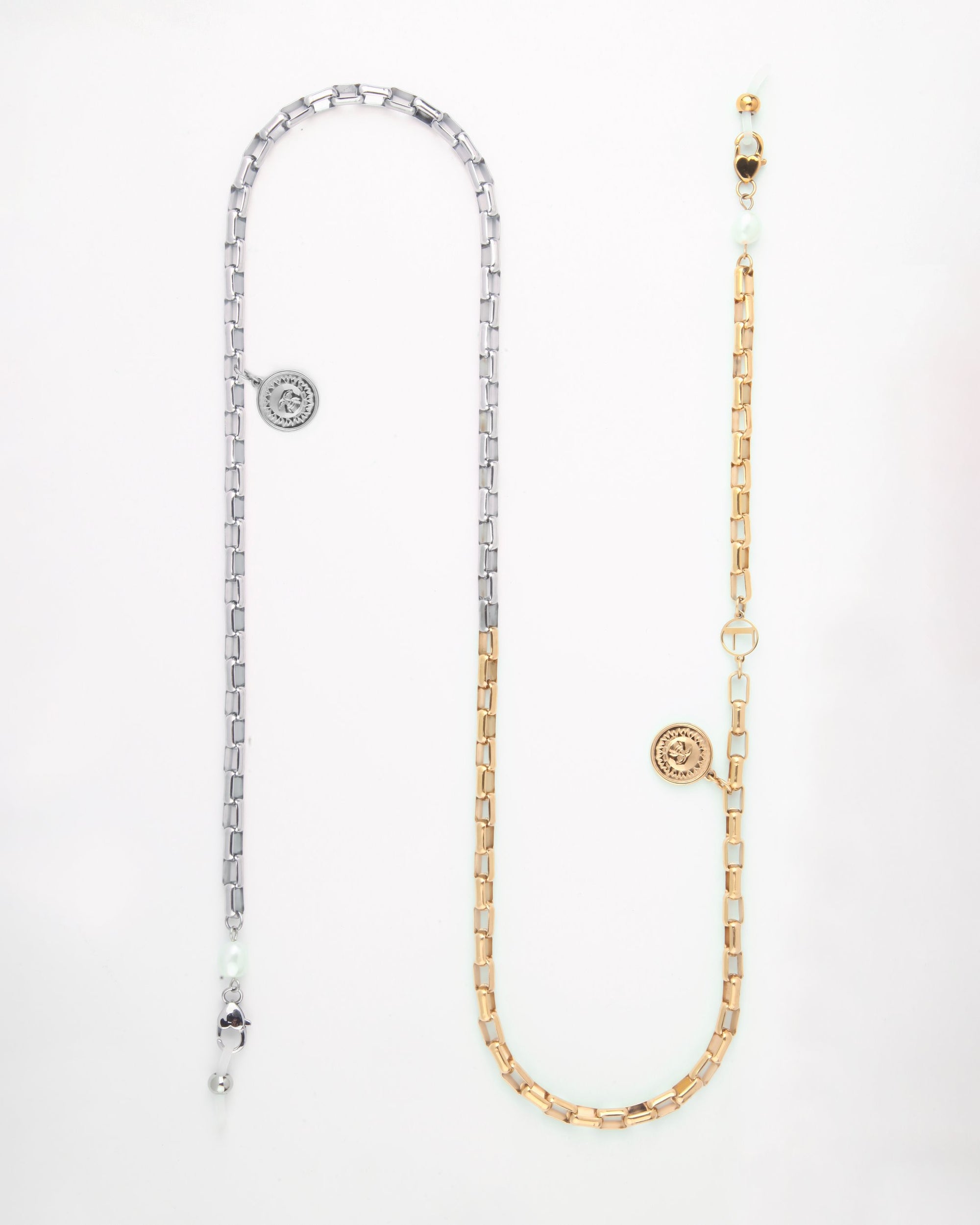 A long, dual-tone glasses chain with two sections: one silver and one gold-toned metal, each featuring rectangular links. Both sections have a round pendant with an intricate design, small white pearls, and a gold circular clasp. This elegant Luna Glasses Chain by For Art's Sake® perfectly balances sophistication and style.