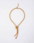 The For Art's Sake® Miller Necklace features a contemporary knot at the front, from which two tassels dangle. One tassel ends with a freshwater pearl pendant, and the other with a small, flat, 18kt gold-plated charm. The necklace is showcased against a plain white background.