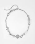 The Sloane Necklace by For Art's Sake® is a silver piece featuring an asymmetrical design with various twisted loops, a crescent moon, a sun with rays, and white pearls. It includes an extension chain for adjustable length and is shown laid flat on a white background.