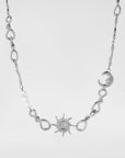 The Sloane Necklace from For Art's Sake® showcases a silver sun pendant at its center, complemented by silver loops and a crescent moon on one side. The left side of the twisted chain is adorned with several small white beads. The length of the necklace is adjustable thanks to an extension chain. It is set against a plain white background.