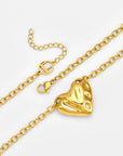 The Sculpted Heart Necklace by For Art's Sake® features a gold chain with a textured, abstract heart-shaped pendant and lobster clasp, plus an extension chain adorned with a small circular cut-out charm.