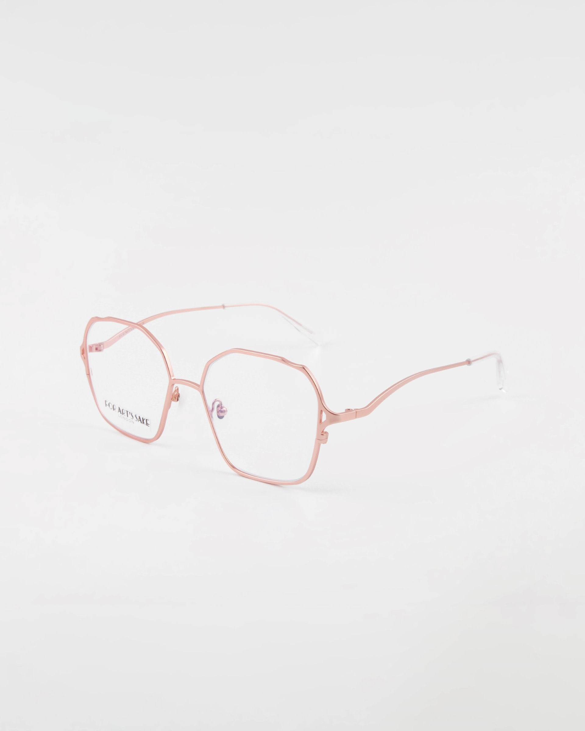 A pair of Mimi eyeglasses by For Art's Sake® with thin, 18-karat gold-plated frames featuring hexagonal lenses, positioned on a white background. The left lens has small printed text reading "L.G.R ARTISANAL.