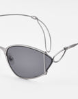 Ornate by For Art's Sake®: Modern almond-shaped sunglasses with dark tinted lenses and a distinctive silver wire frame featuring an artistic looped design near the temple for vintage-inspired flair.