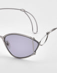 A close-up of For Art's Sake® Ornate sunglasses featuring a modern almond shape, edgy metal frame, and light purple-tinted lenses, set against a plain white background.