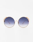 A pair of For Art's Sake® Lindy handmade gold-plated round sunglasses with ultra-lightweight shatter-resistant dark blue gradient lenses. The bridge and end pieces have a decorative floral embellishment, offering 100% UVA & UVB protection. The For Art's Sake® Lindy sunglasses are set against a plain white background.