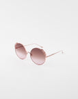 A pair of stylish round sunglasses with ultra-lightweight shatter-resistant pink-tinted lenses and rose gold frames featuring floral detailing on the upper rims, offering 100% UVA & UVB protection, the Lindy by For Art's Sake®.