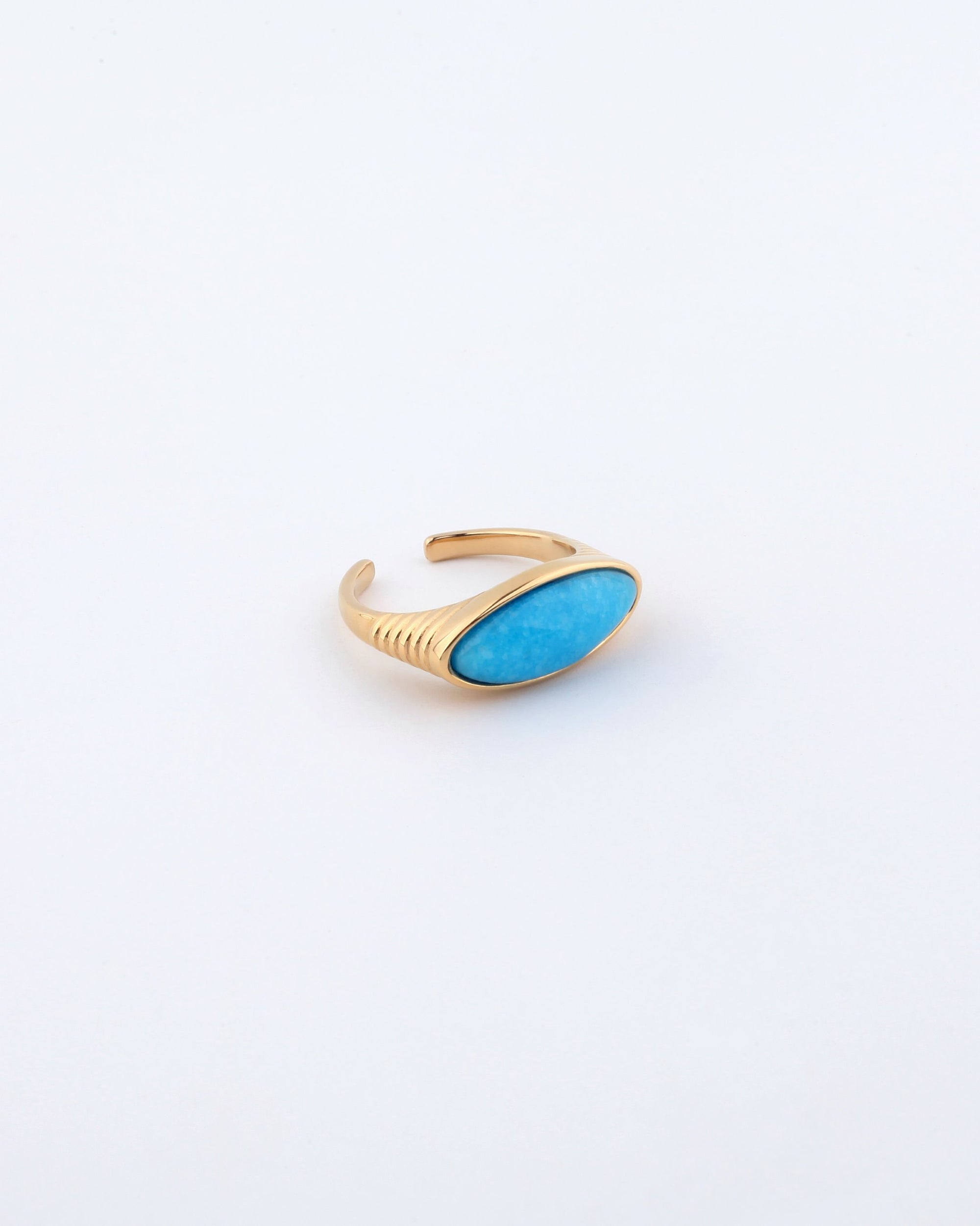 The Enza Ring from For Art's Sake® features a gold-plated stainless steel open band design, adorned with an oval-shaped turquoise gemstone set on top. The piece is displayed against a plain white background, accentuating its polished enamel finish.
