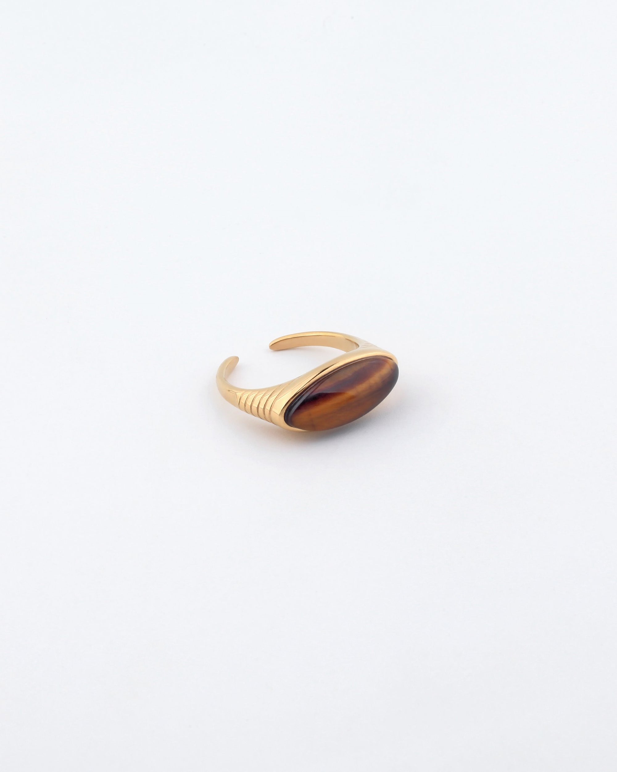 The For Art's Sake® Enza Ring, made from gold-plated stainless steel, showcases an oval-shaped brown gemstone set against a plain white background. Its open back and polished enamel finish complement its elegant and minimalist design.