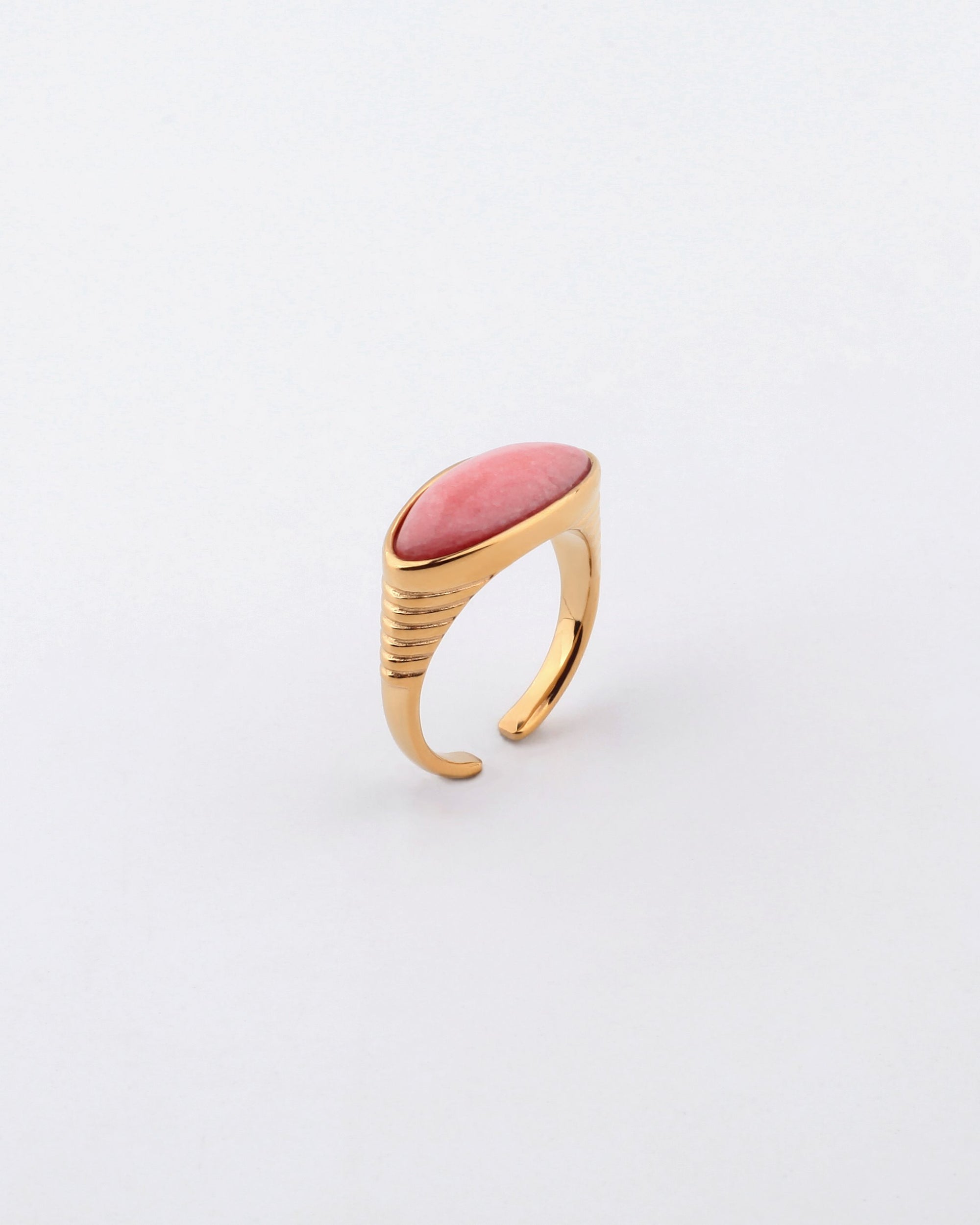 The Enza ring by For Art's Sake® is a gold open-ended piece featuring an elongated oval coral-colored stone set horizontally at the top. Crafted from gold-plated stainless steel, it boasts a minimalist design with a polished finish and subtle ridged detailing on the band near the stone, set against a white background.