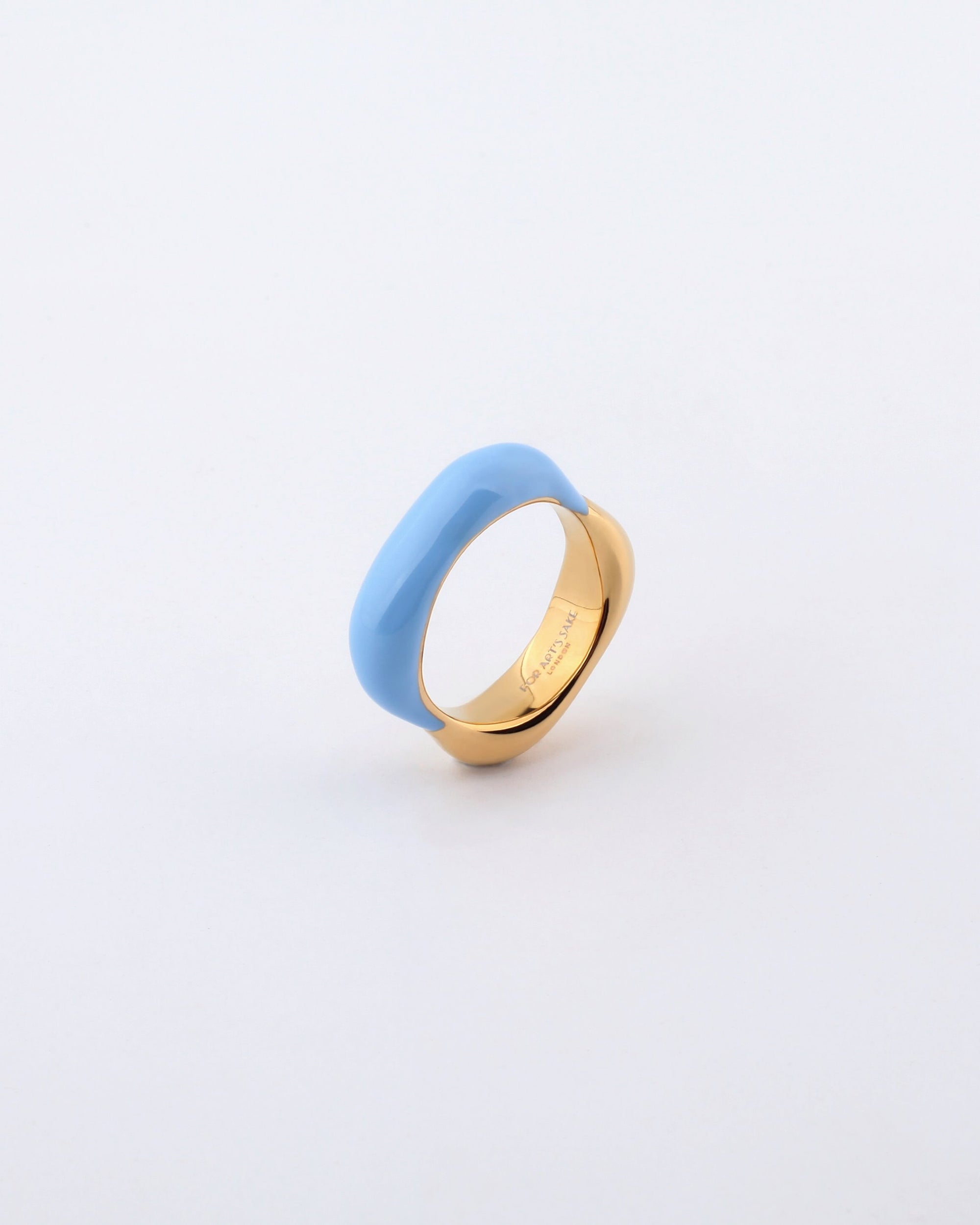 The Raya Ring by For Art's Sake® features a gold-toned metal base with a glossy blue oval-shaped top and an inscription of "Souvenir" engraved inside. The understated white background perfectly accentuates the ring's design.