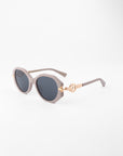 A pair of stylish Seaside, round sunglasses with dark, shatter-resistant lenses and light grey handmade acetate frames from For Art's Sake®. The arms feature a decorative gold-colored accent near the hinges. They are placed on a plain white surface.