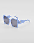 The Eos - Blue sunglasses by For Art's Sake® feature square blue frames with an oversized soft-square silhouette and dark lenses, shown on a white background angled to display both the front and side. (ONLY 2 LEFT).