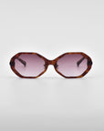 Front view of a pair of Lotus sunglasses by For Art's Sake® with an angular silhouette, featuring tortoiseshell frames and pink-tinted lenses, complemented by jade-stone nose pads. The sunglasses are placed on a plain white background.