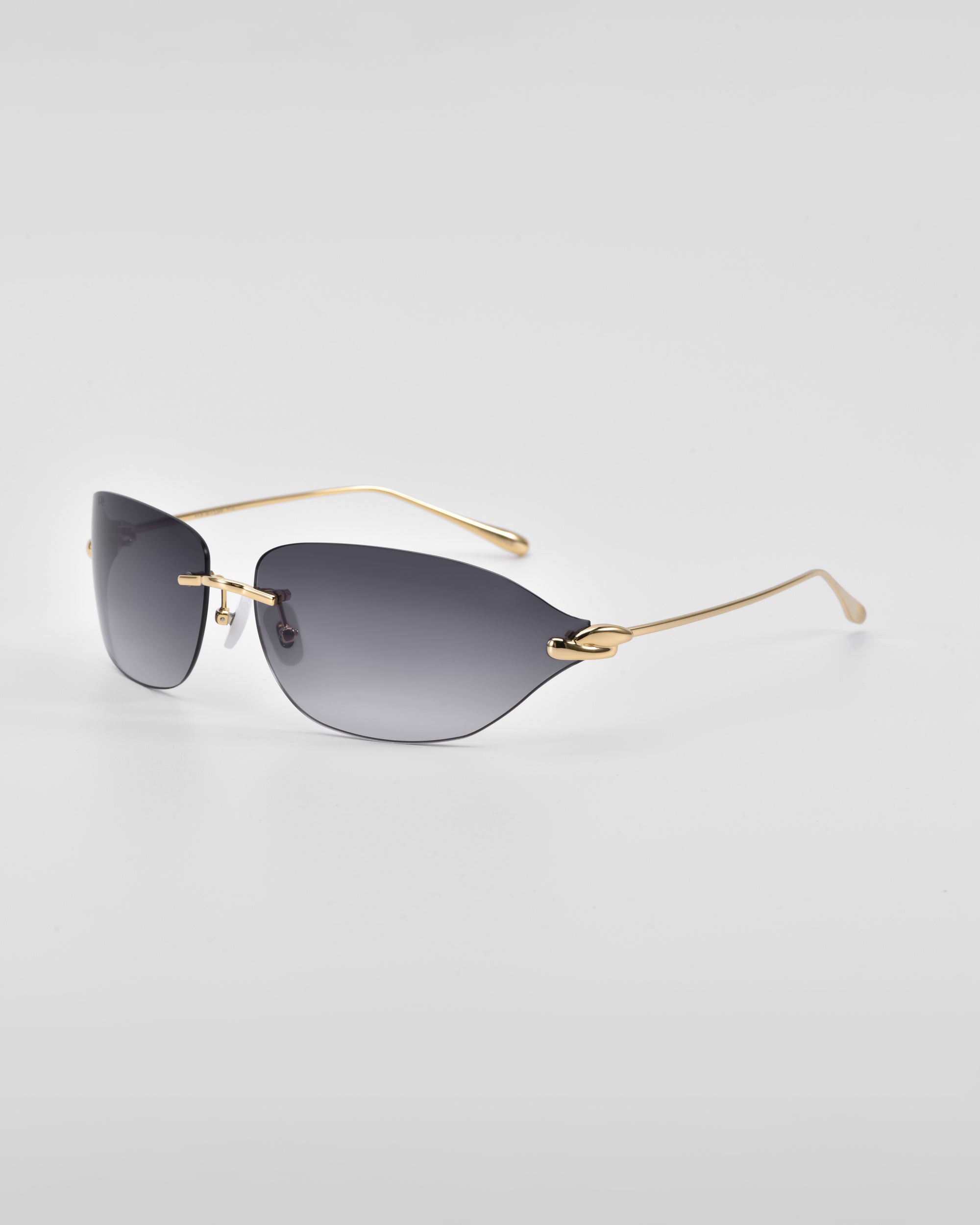 A pair of stylish For Art's Sake® Serpent I rimless sunglasses with dark tinted lenses and golden thin arms, photographed on a white surface. The minimalistic design, featuring 18-karat gold plating, gives them a sleek, modern look.
