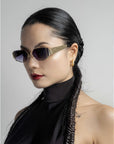 A woman with sleek, braided hair wears For Art's Sake® Talia gold-plated, full metal frame sunglasses, gold hoops, a sleeveless black top, and red lipstick while posing against a plain light background.