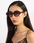 A woman with long, straight, dark hair is wearing oversized almond-shaped Vera sunglasses by For Art's Sake® and a black lace camisole. She has a neutral expression and is posed against a plain white background.