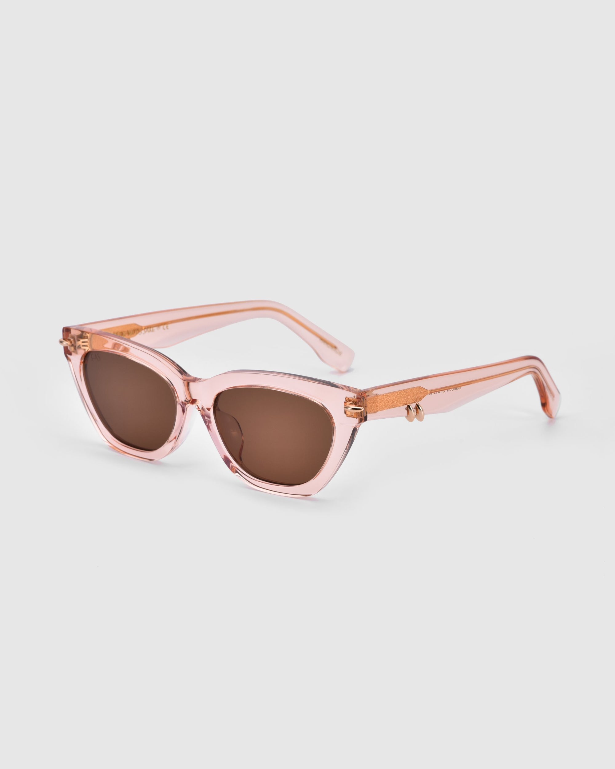 A pair of For Art's Sake® Bonbon sunglasses with dark lenses and thick, transparent pink frames. The arms of the sunglasses feature a matching design with small gold accents on the hinges, adding a touch of flair. The image showcases these chic accessories against a plain white background.