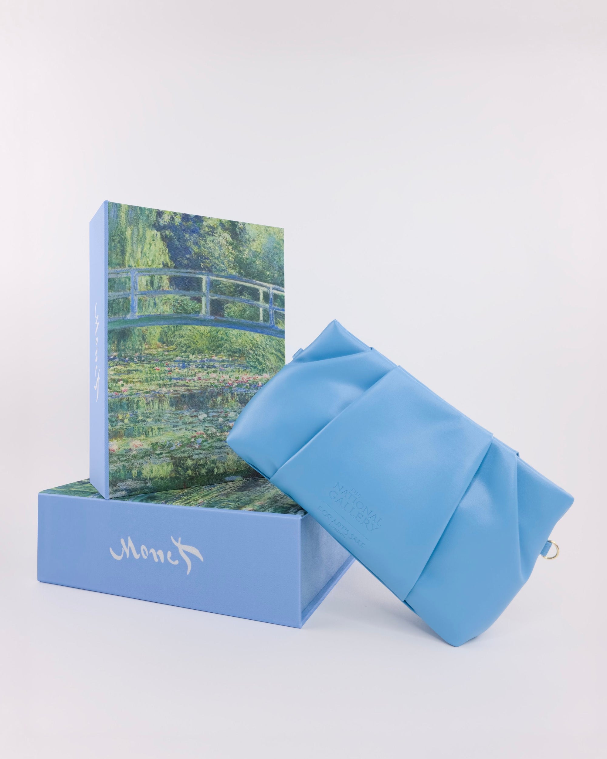 A light blue clutch bag sits beside two stacked boxes: a blue “Claude Monet” box and an upper box with Monet-inspired art from For Art’s Sake®, revealing exclusive limited edition sunglasses.
