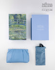 A flat lay features a Monet art book, light blue box, clutch, and suede pouch with limited edition Claude Monet sunglasses by For Art's Sake®—all set on a white background.