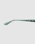 The Claude Monet by For Art's Sake® is a long, thin, blue-green eyewear piece with a curved, flattened end and a weathered surface, set against a plain white background for an artistic touch.