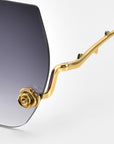 Close-up of La Vie En Rose sunglasses by For Art's Sake®. The gold frame intricately mimics a rose stem with sculpted rose ornaments on the arms, and gradient lenses transition elegantly from dark to light.
