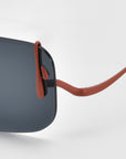 Close-up of For Art's Sake® Vermilion sunglasses, showcasing rectangular dark lenses and slim red-brown temples with distinctive dripping metal accents, set against a white background.